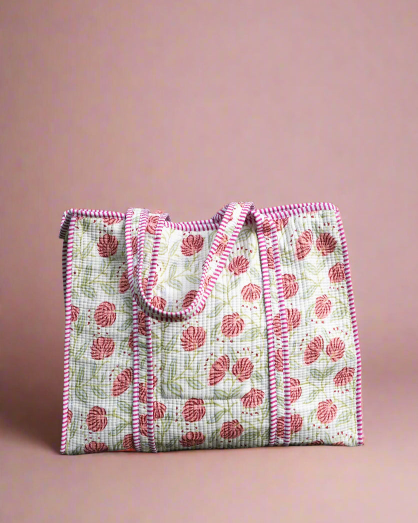 Handmade quilted bag with pink floral pattern on a stone surface with greenery in the background