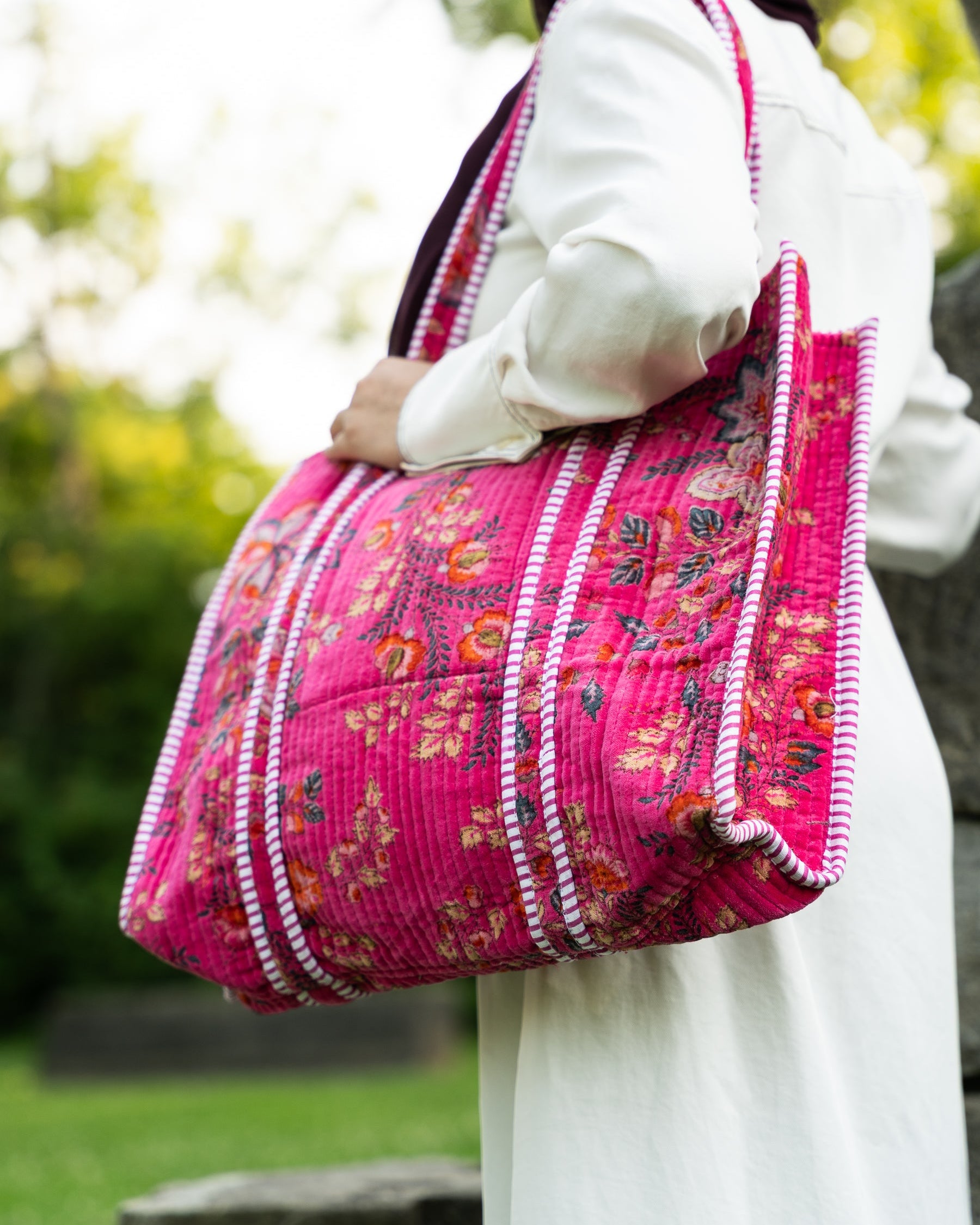 Person holding a pink floral handbag with a blurred outdoor background