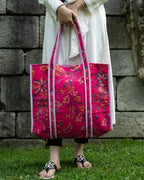 Person holding a pink floral tote bag against a stone wall background