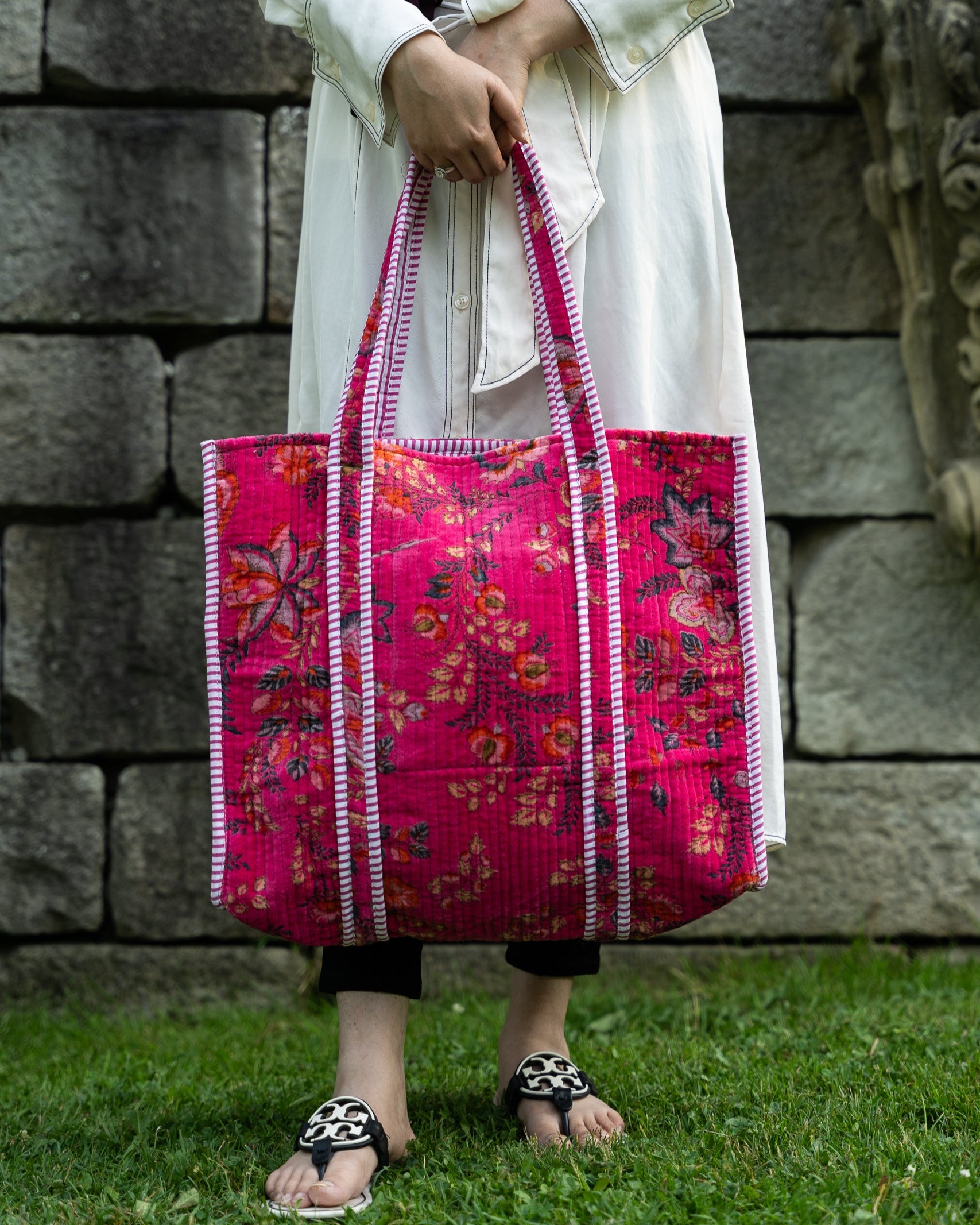 Person holding a pink floral tote bag against a stone wall background