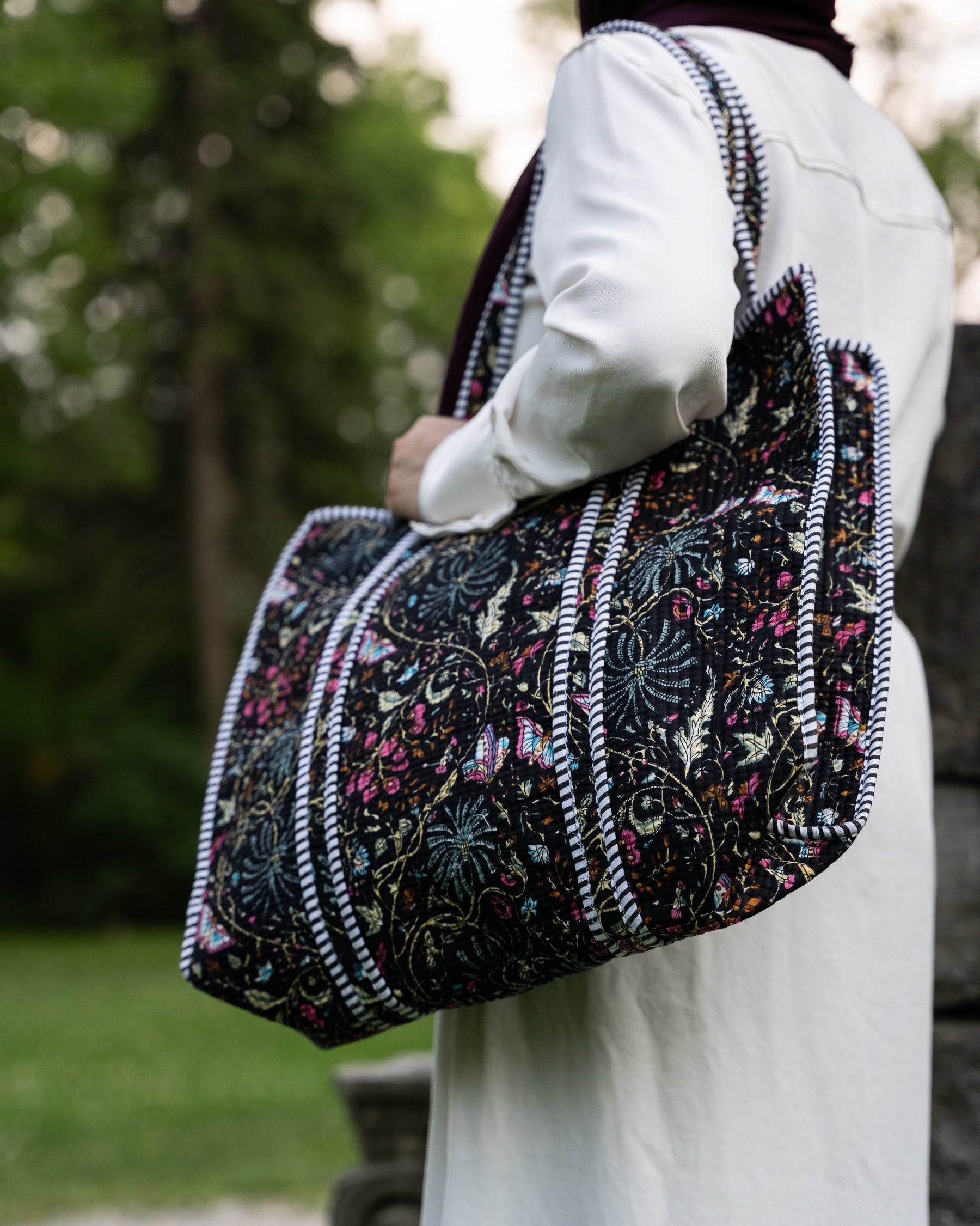Person holding a patterned bag outdoors with blurred greenery in the background