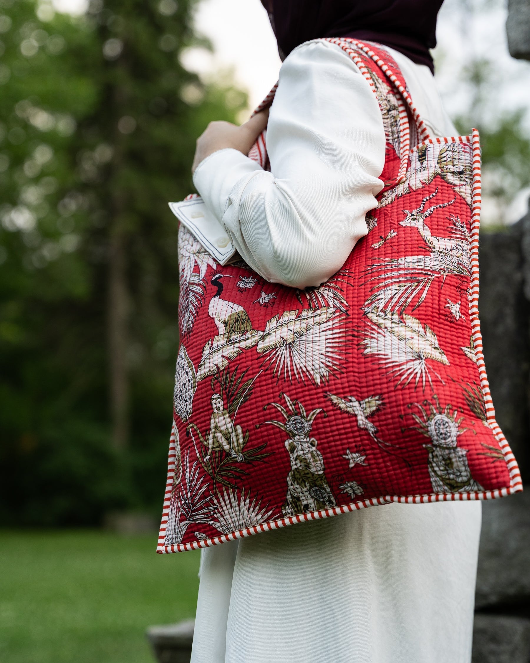 Person wearing a red patterned vest outdoors with greenery in the background