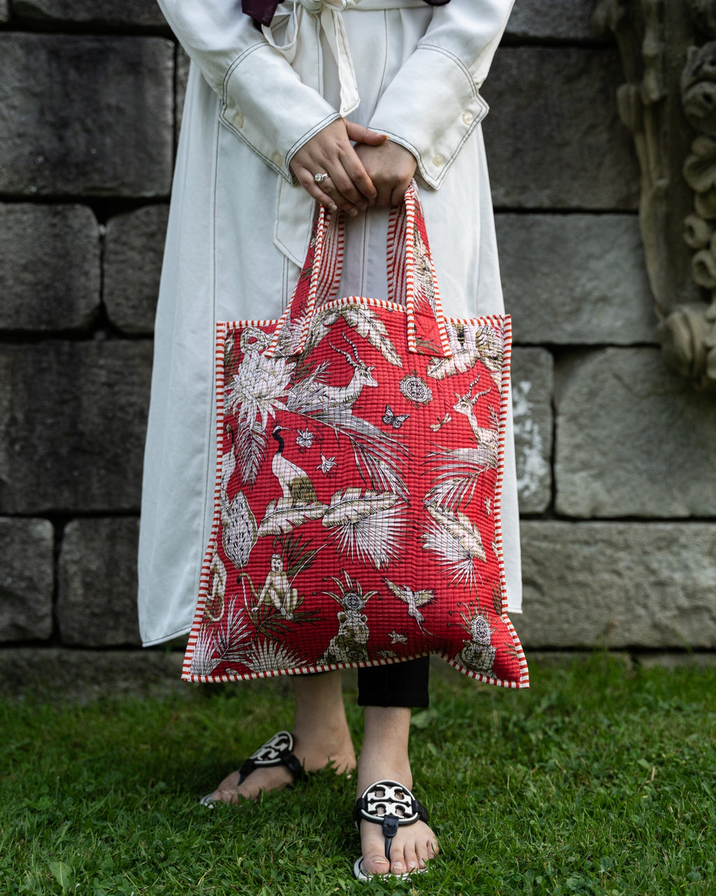 Person holding a red embroidered bag against a stone wall.