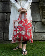 Person holding a red embroidered bag against a stone wall.