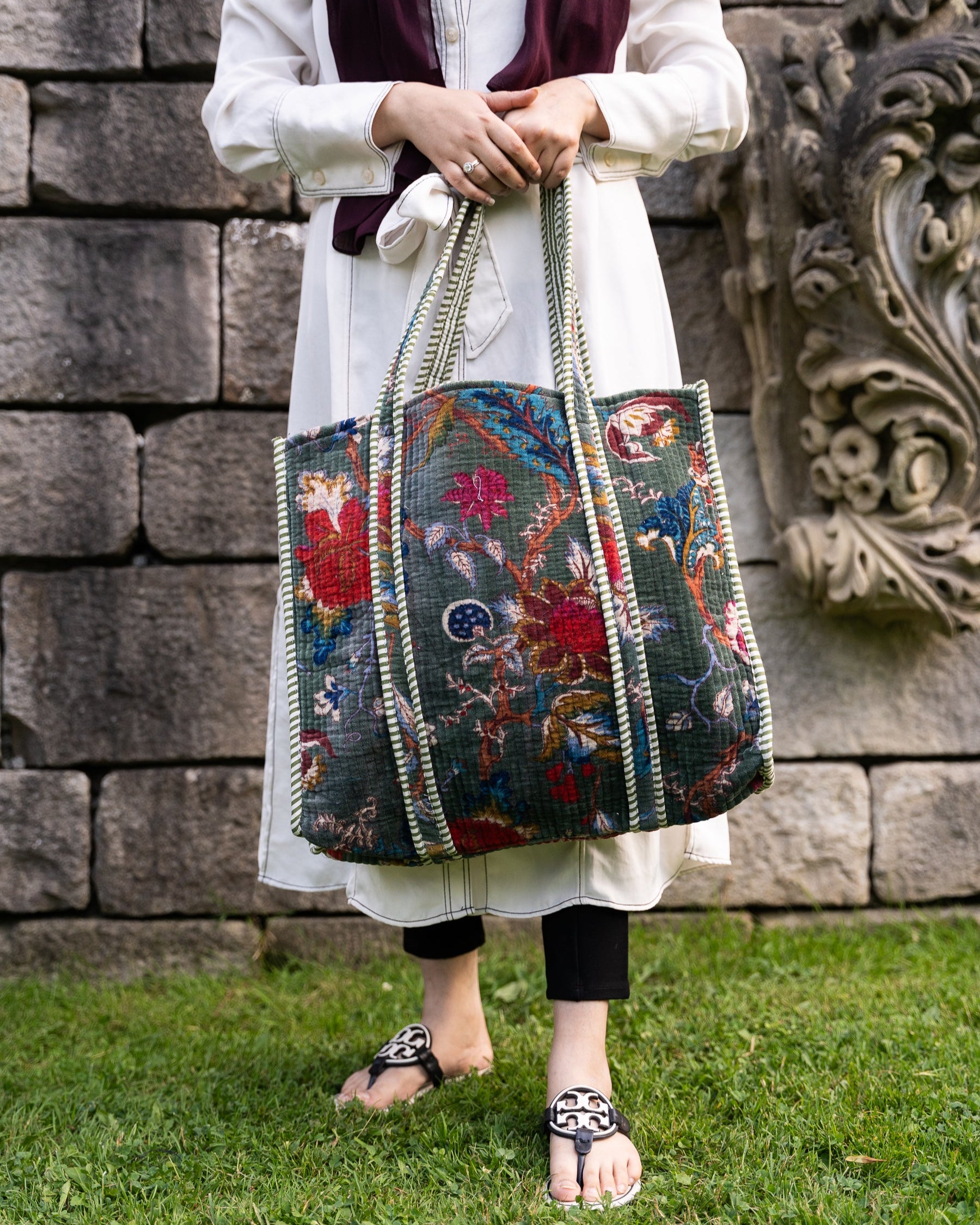 Person holding a colorful patterned bag against a stone wall background
