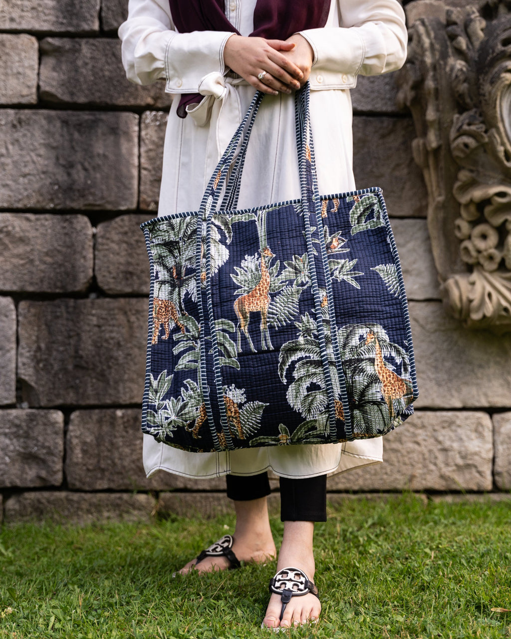 Person holding a navy blue tote bag with animal prints against a stone wall.