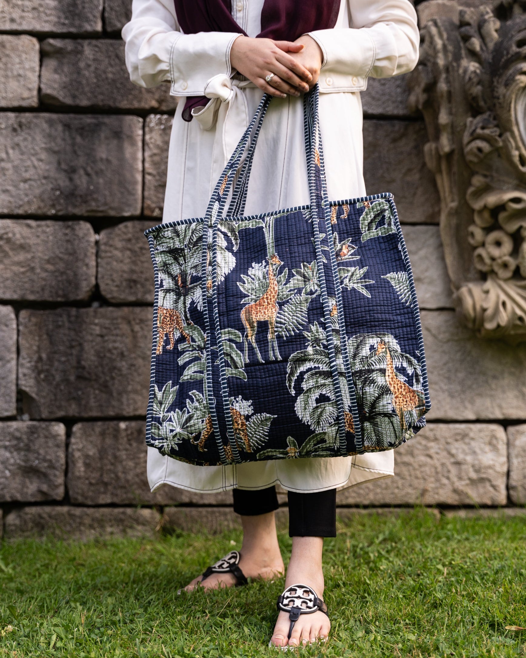 Person holding a navy blue tote bag with animal prints against a stone wall.
