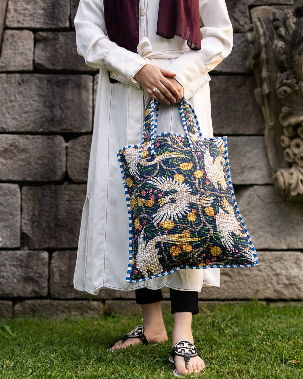 Person holding a patterned bag against a stone wall background