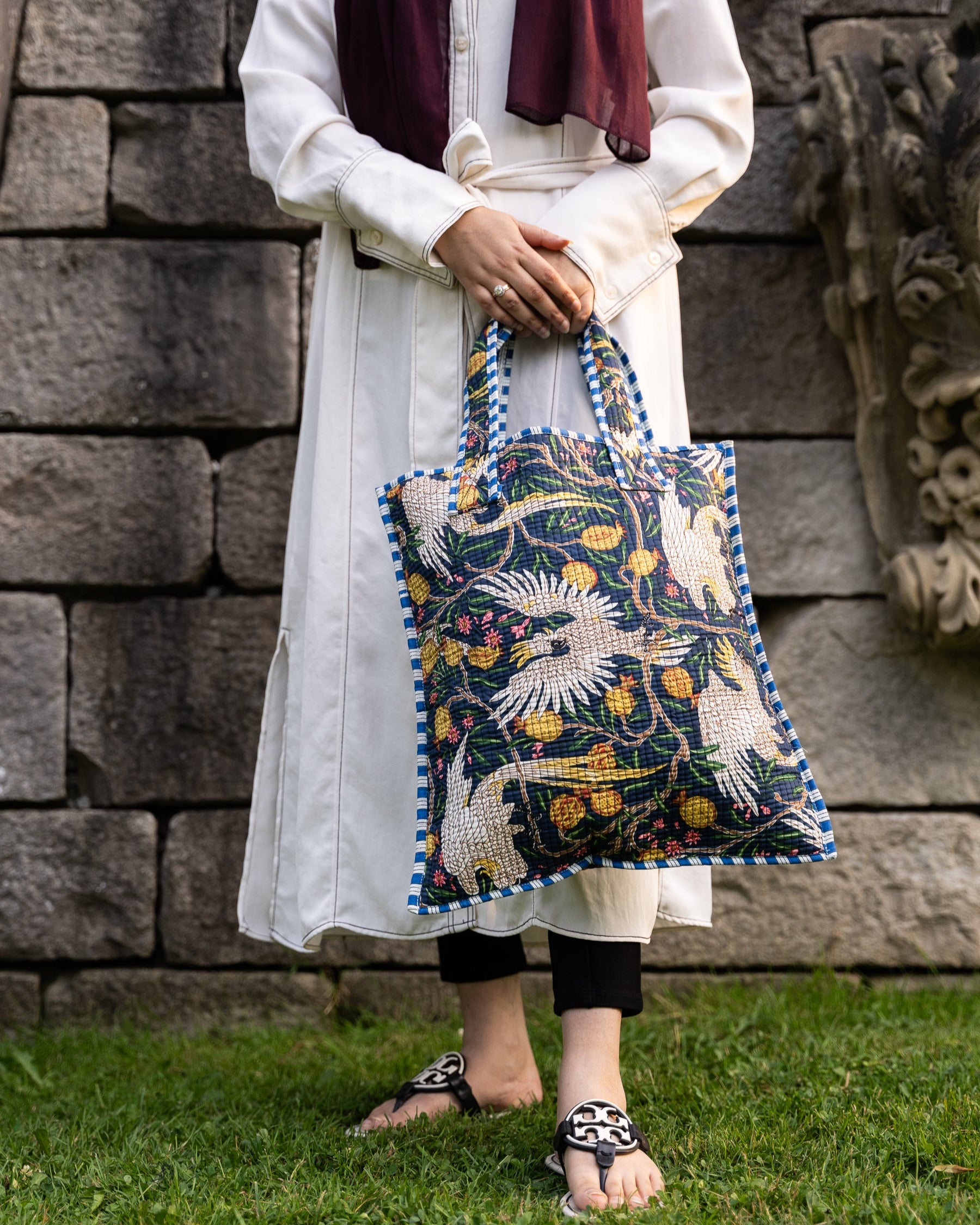 Person holding a patterned bag against a stone wall background