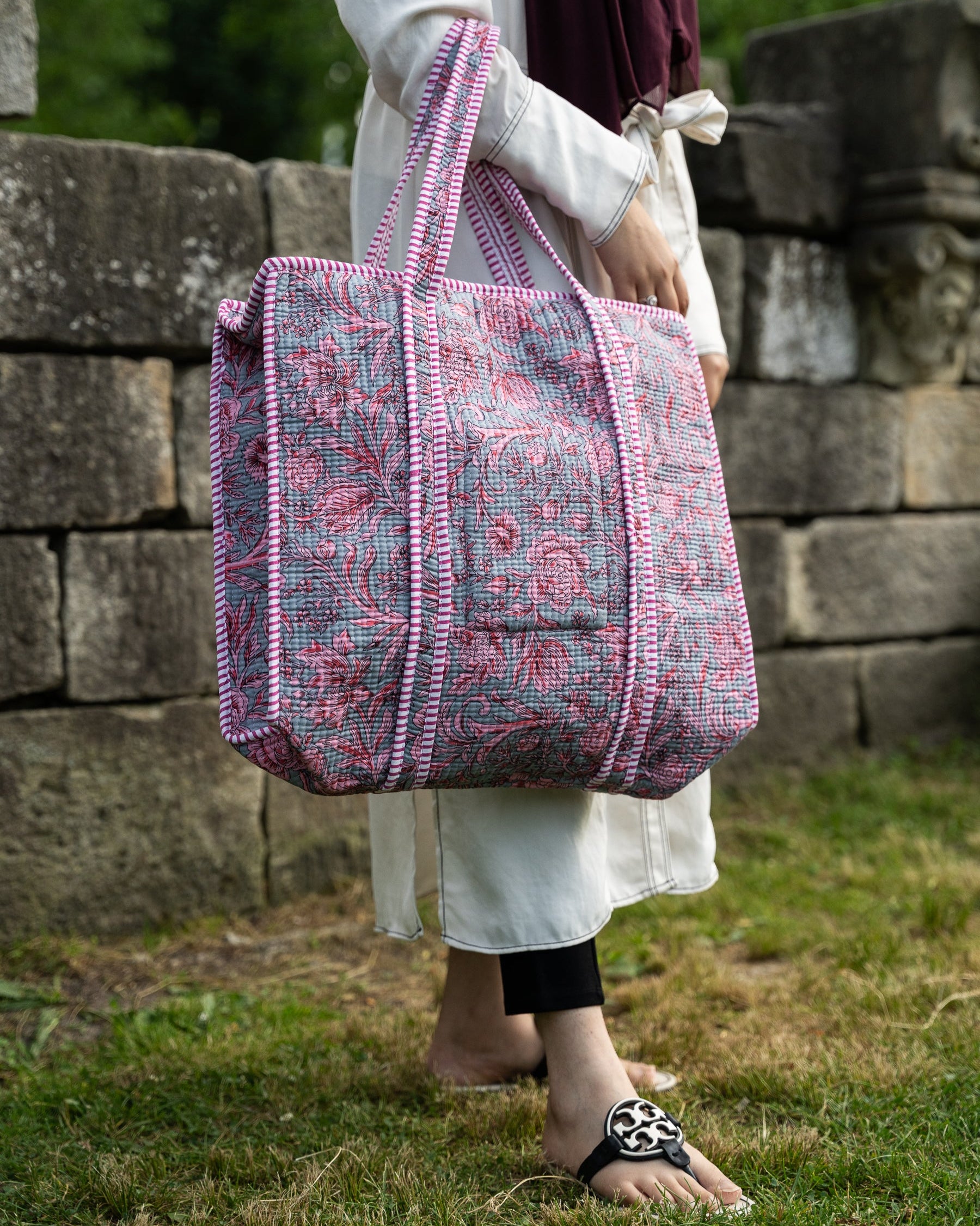 Person holding a pink and gray patterned bag outdoors near stone walls.