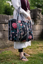 Person holding a floral-patterned bag outdoors near a stone wall.