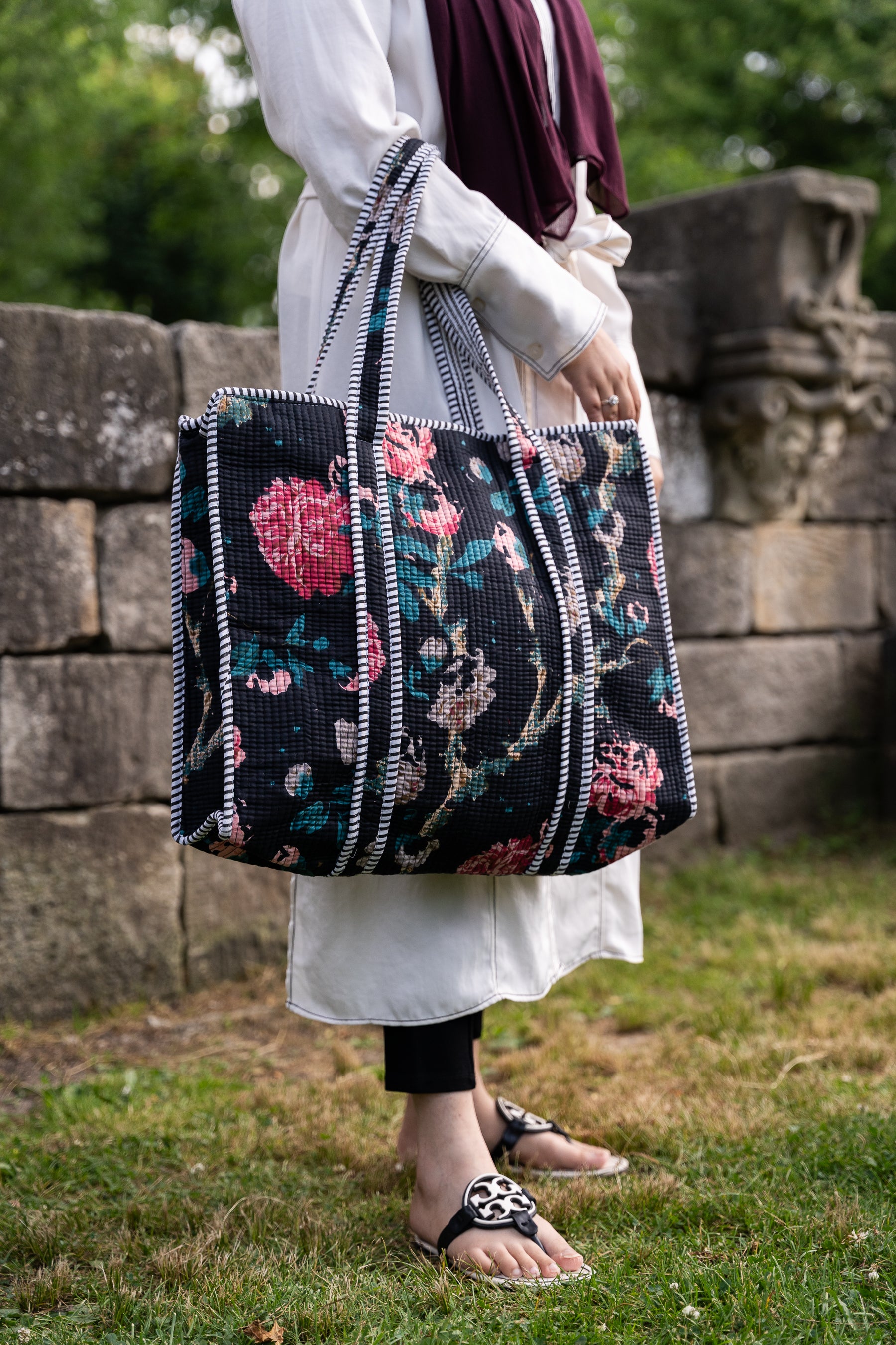 Person holding a floral-patterned bag outdoors near a stone wall.