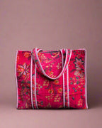 Pink floral tote bag on a stone surface with greenery in the background