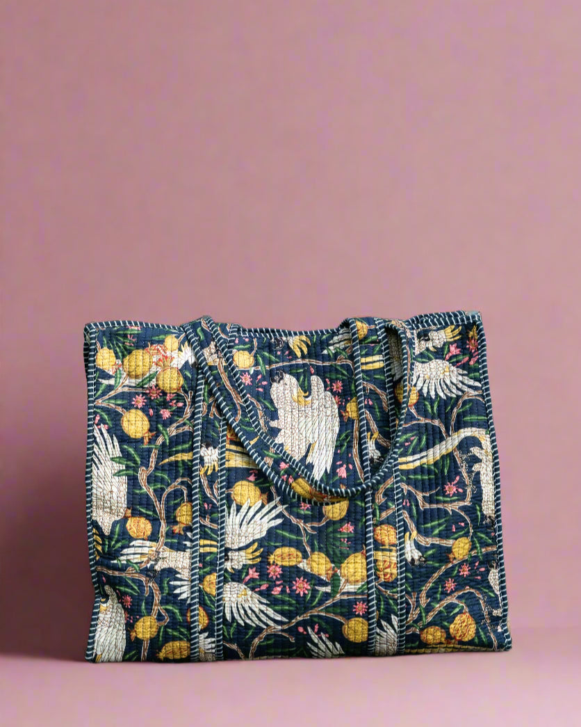 Embroidered fabric pouch with floral and bird patterns on a stone surface with greenery in the background