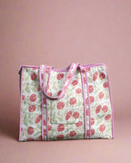Handmade quilted bag with pink floral pattern on a stone surface with greenery in the background