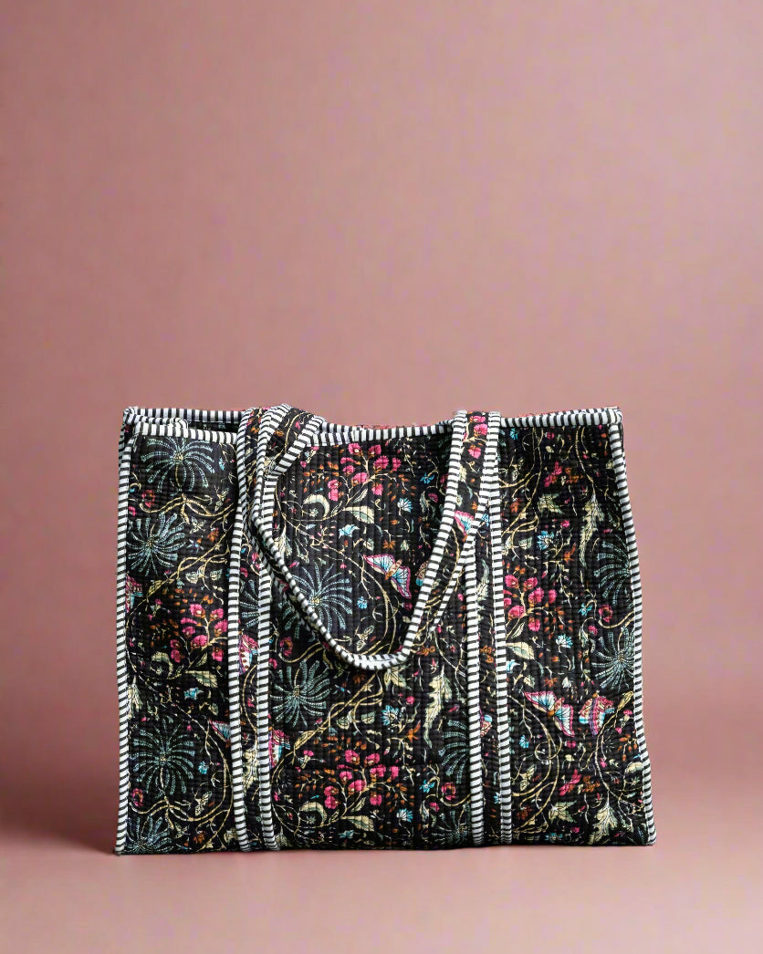 Floral patterned bag with black and white trim on a stone surface with greenery in the background