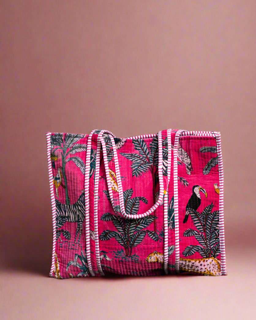 Pink embroidered bag with bird patterns on a stone surface with greenery in the background