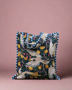 Decorative pillow with floral and bird pattern against a stone wall.
