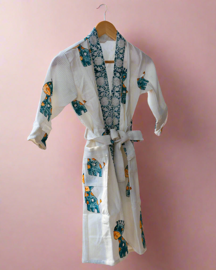 White robe with floral patterns hanging on a wooden rack against a neutral wall.