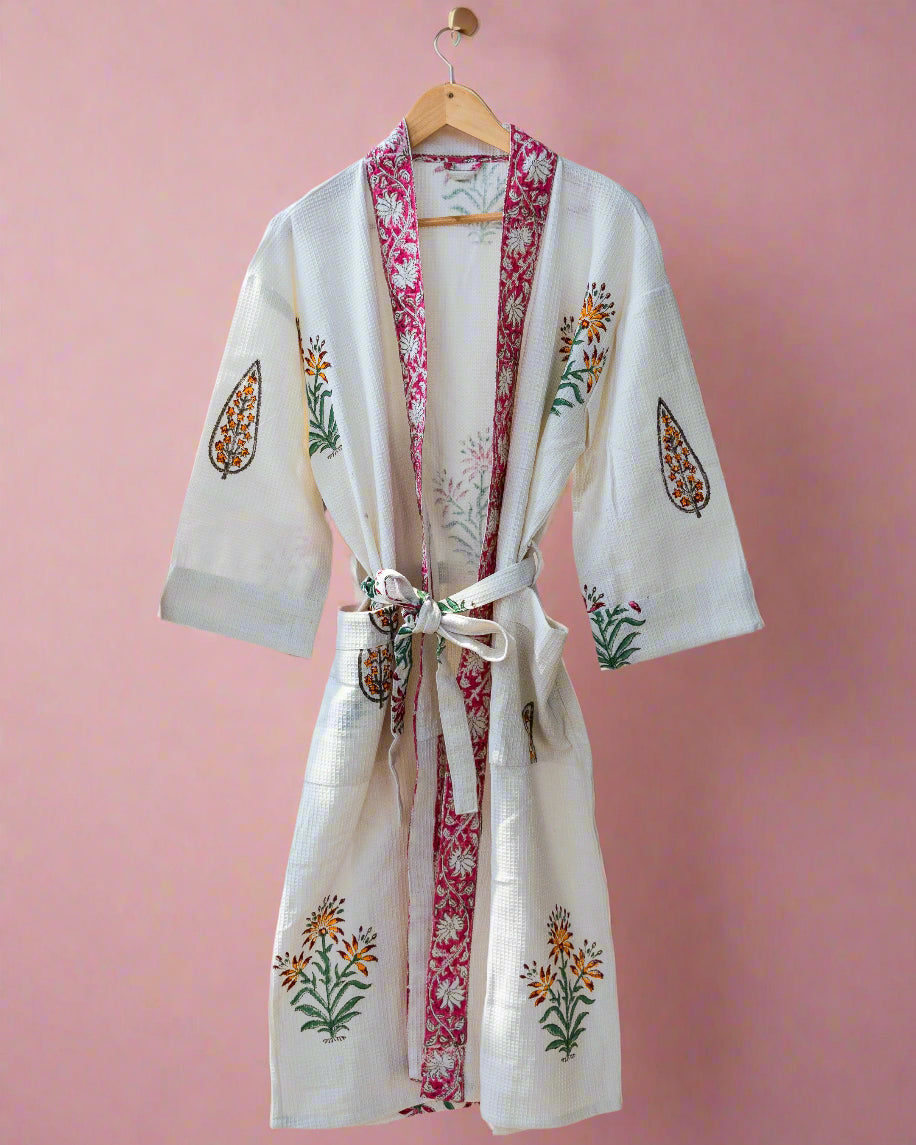 White embroidered robe with floral patterns hanging on a wooden rack.